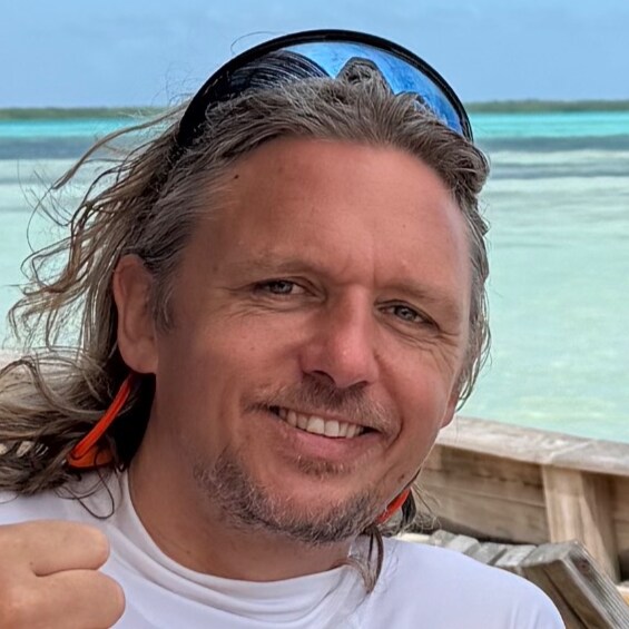 Siemme, tu anfitrión, sonriendo en un barco con el mar turquesa de Bonaire detrás